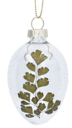 Two clear glass ornaments with pressed green leaves and white flowers on a white background