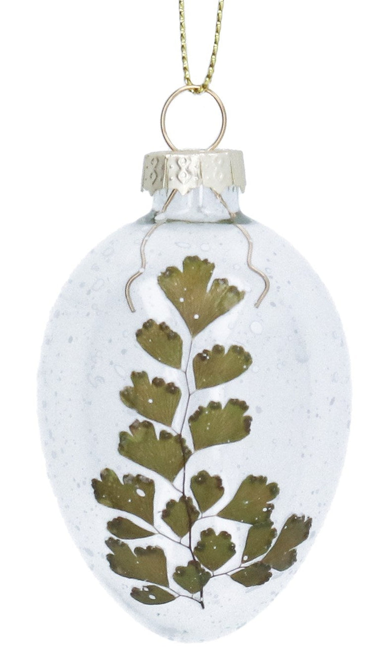 Two clear glass ornaments with pressed green leaves and white flowers on a white background