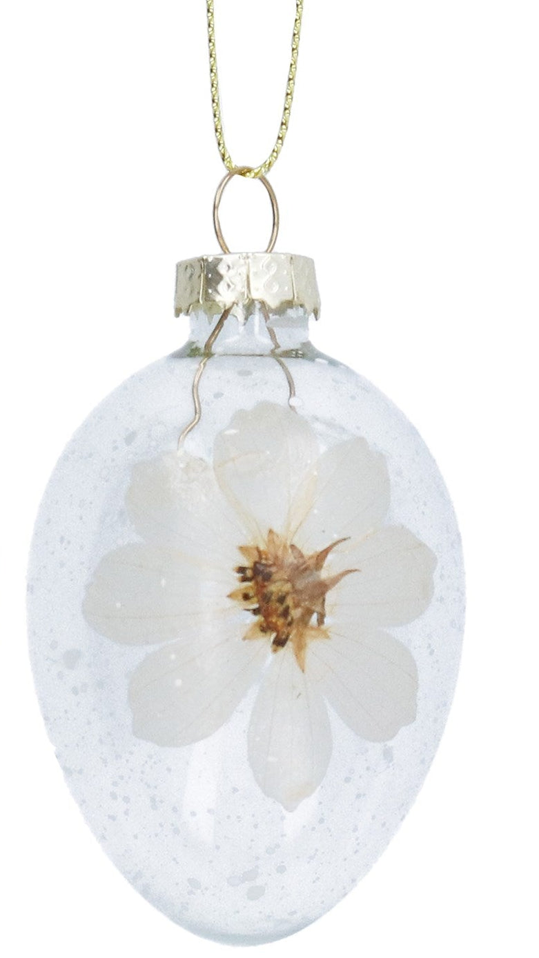 Two clear glass ornaments with pressed green leaves and white flowers on a white background