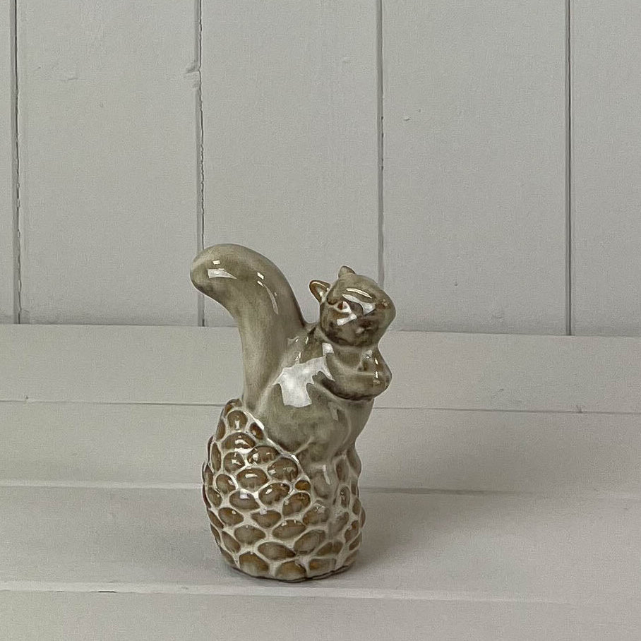 Beige mottled ceramic squirrel sitting on an pinecone decoration